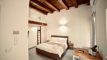 A bedroom with a bed, bedside table, and a desk with a chair. There is a ladder against the wall and a wall-mounted phone.