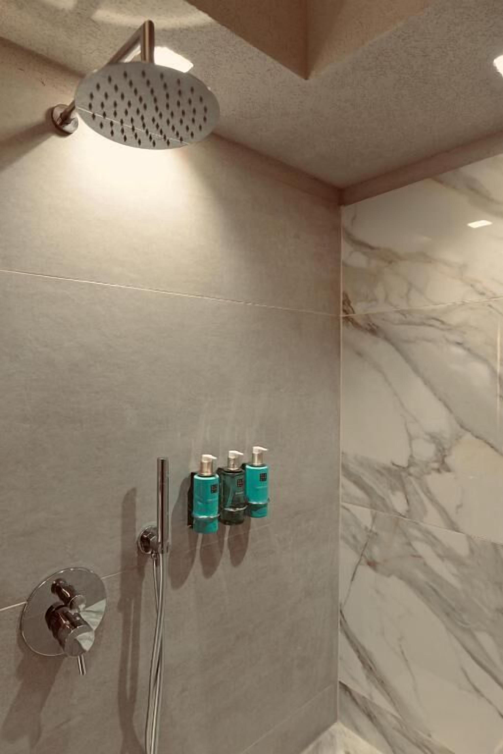 A shower with a handheld showerhead, a wall-mounted faucet, and two wall-mounted soap dispensers.