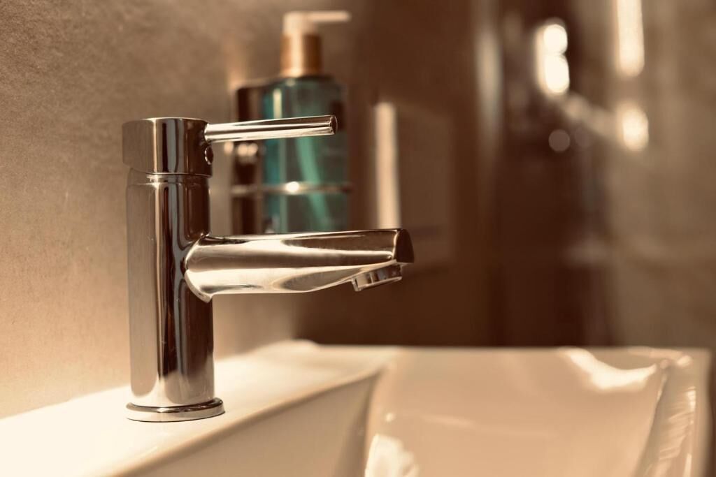 Un baño moderno con un grifo cromado, un lavabo blanco y una botella azul al fondo.