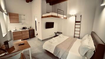 Habitación de hotel pequeña con literas, kitchenette, televisor de pantalla plana y escritorio de madera.