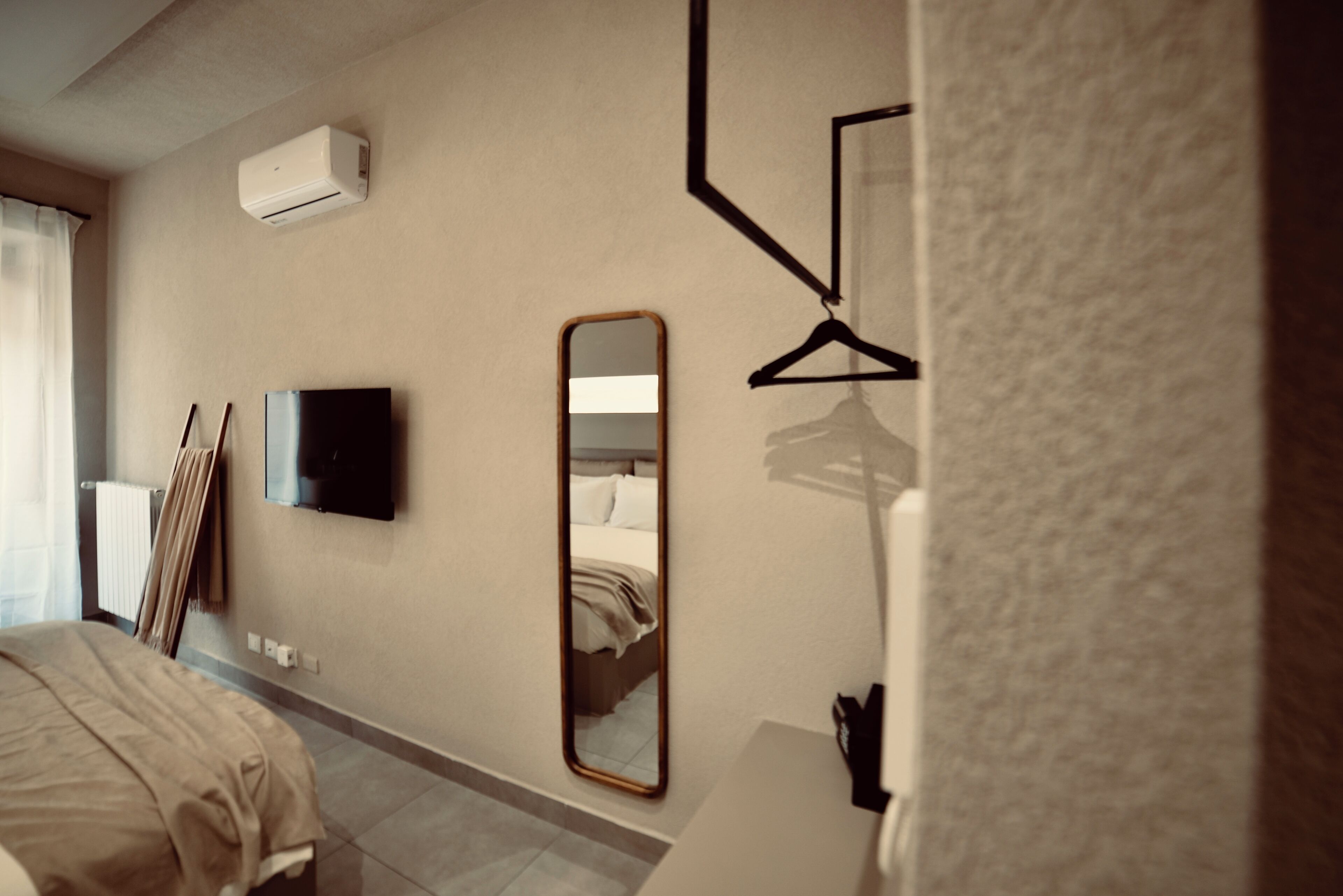 A hotel room with a bed, a flat-screen TV, a wall-mounted mirror, and a black hanger.