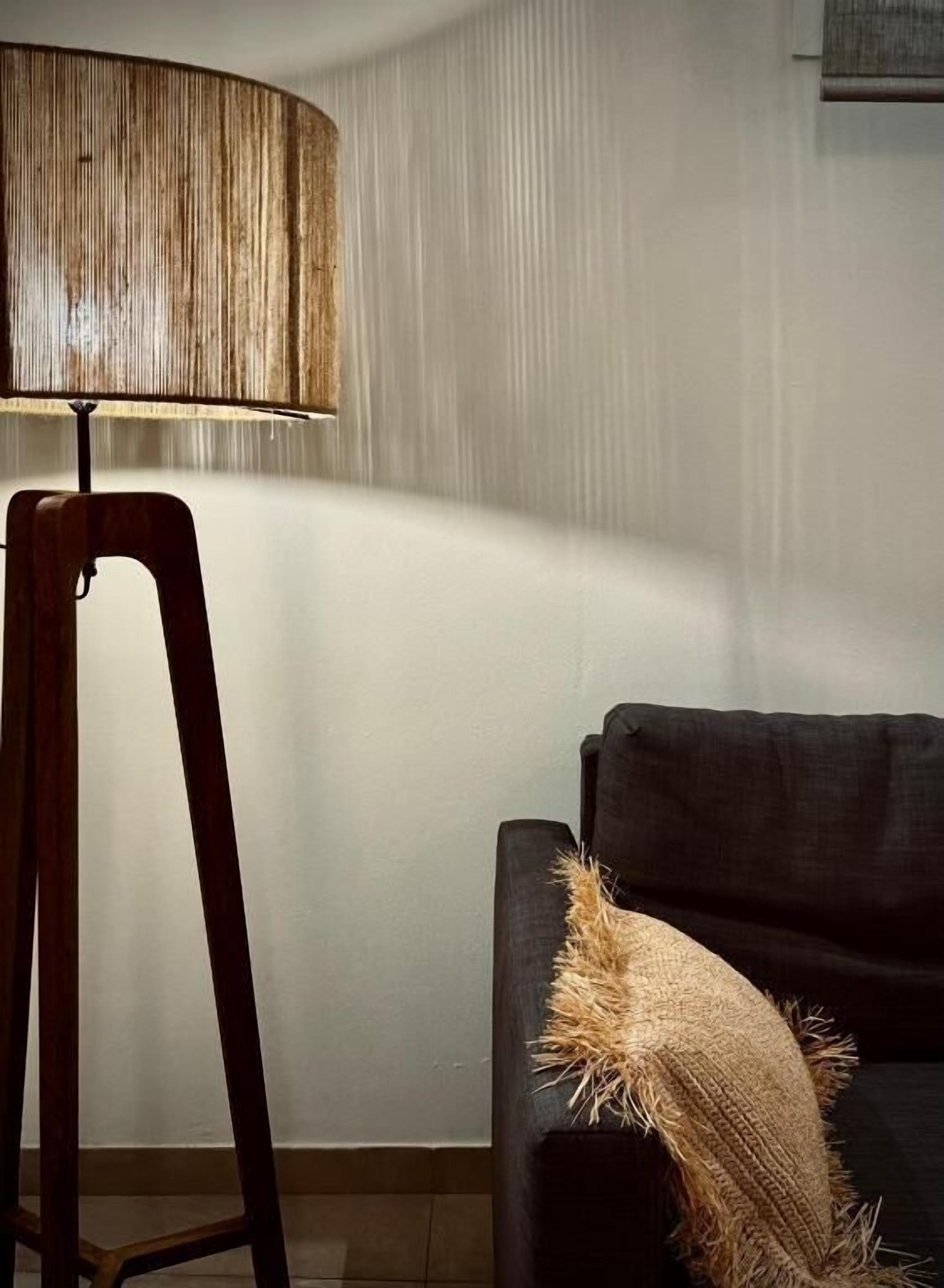 Un racó d'una habitació amb una làmpada de peu de fusta i un sofà fosc amb una manta amb textura.