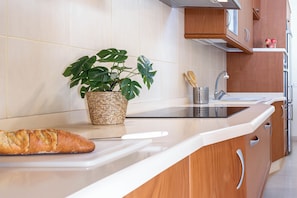 Une cuisine avec un plan de travail blanc, une miche de pain, une plante en pot et des meubles de rangement en bois.