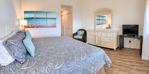 Un dormitorio con cama, cómoda, televisor y una obra de arte en la pared.