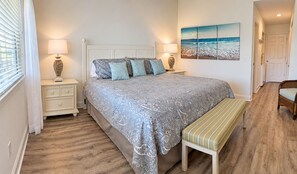 A bedroom with a bed, bedside tables, a bench, a painting, and a door.