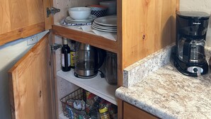 Eine Küche mit Holzausstattung, einer Kaffeemaschine und verschiedenen Küchenutensilien auf Regalen.