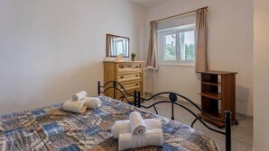 Une chambre à coucher avec un lit, une commode en bois, un miroir et une fenêtre avec des rideaux.