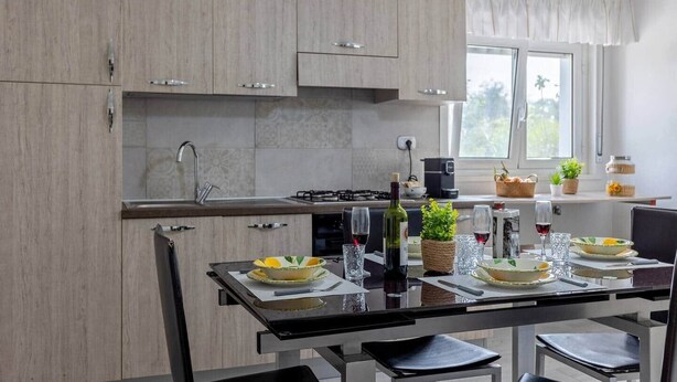Une cuisine moderne avec des meubles de couleur bois clair, un îlot central doté de sièges, une cuisinière à gaz et une fenêtre avec des rideaux.