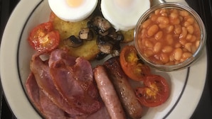Een bord met ontbijt, inclusief eieren, worstjes, tomaten, bonen en ham.