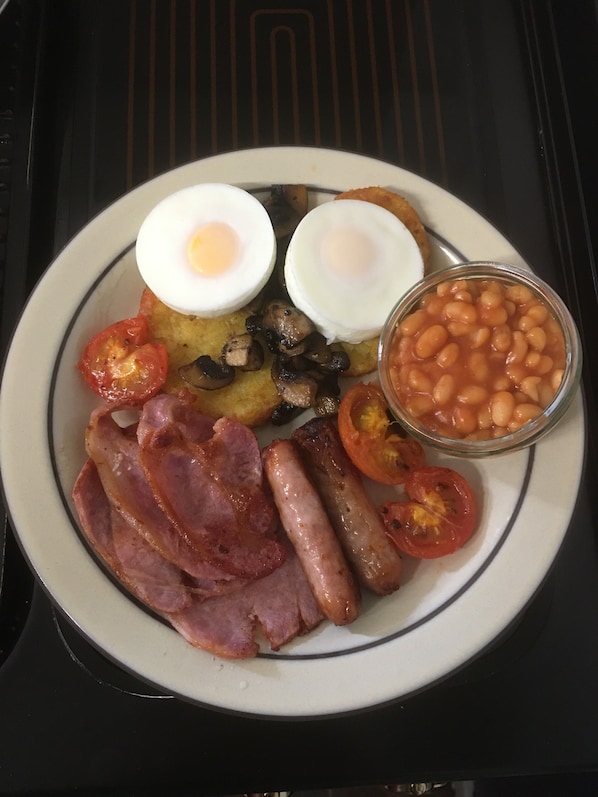 Ein Teller Frühstück mit Eiern, Würstchen, Tomaten, Bohnen und Schinken.