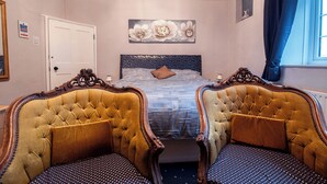 Een slaapkamer met een groot bed, twee gestoffeerde fauteuils, een decoratief hoofdeinde en een raam met gordijnen.