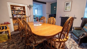 Een eetkamer met een houten tafel en stoelen, een boekenkast, een open haard en een lijst met een afbeelding aan de muur.