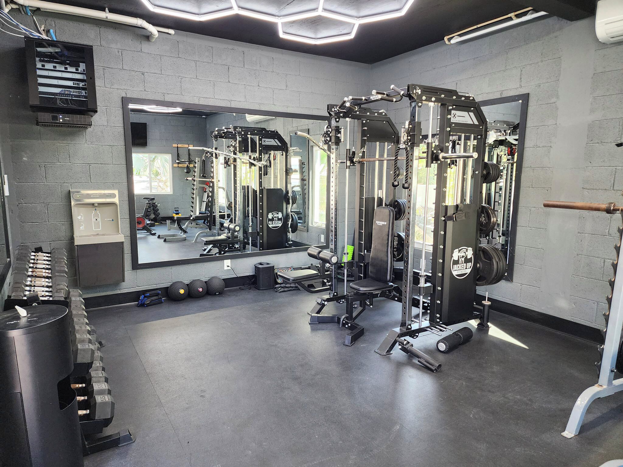A gym with weightlifting equipment, a mirror, and a wall-mounted electrical box.