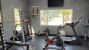 Ein Fitnessstudio mit vielfältigen Geräten, darunter eine Hantelbank, ein Squat-Gestell und Laufbänder.