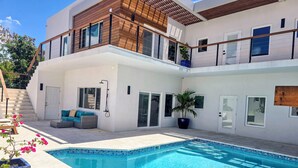 Ein modernes, zweigeschossiges Haus mit Swimmingpool, Sitzgelegenheiten im Freien und einer Treppe, die zum Obergeschoss führt.