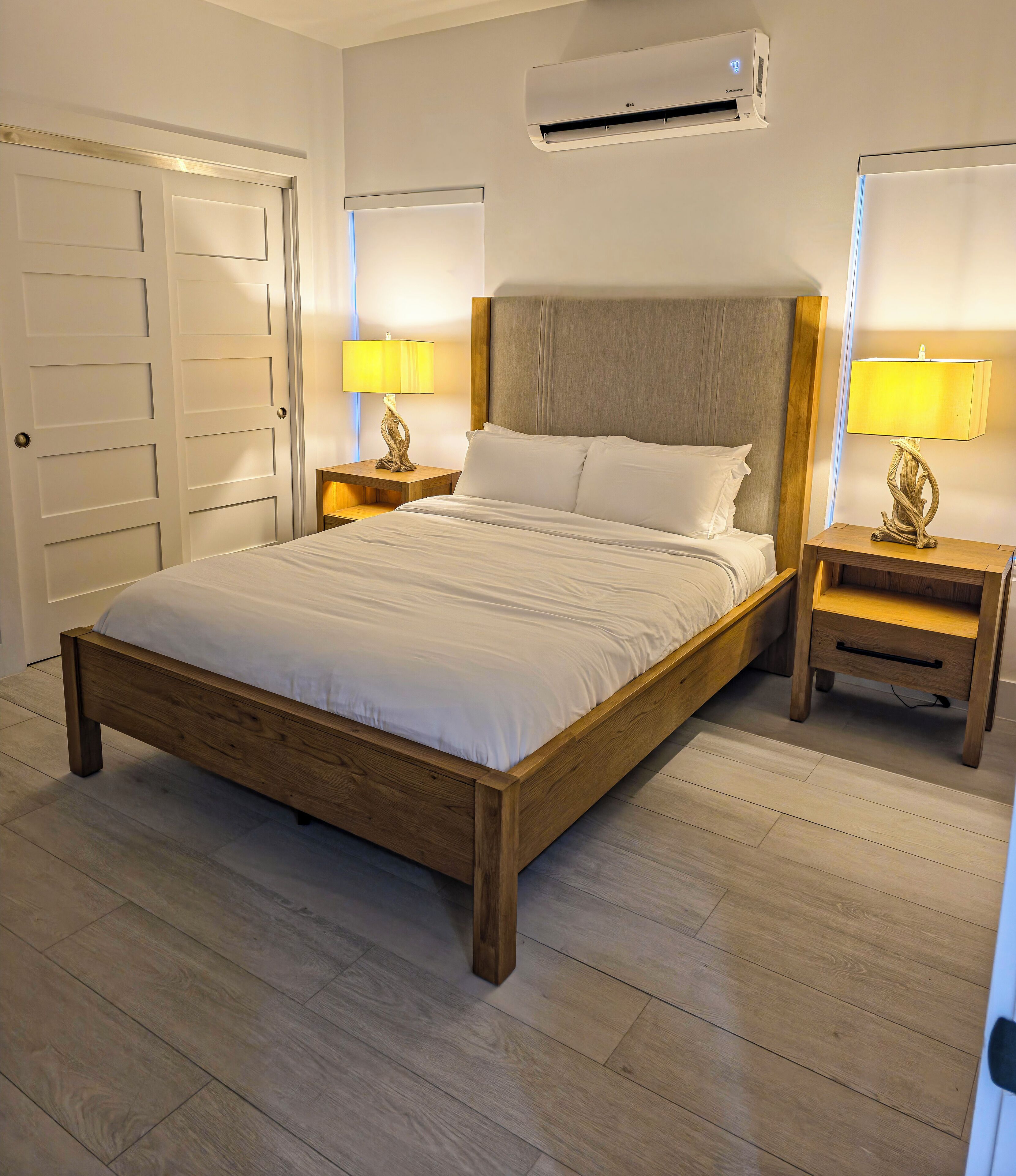 Une chambre à coucher avec un lit en bois, deux tables de chevet avec des lampes, un appareil de climatisation et une porte.