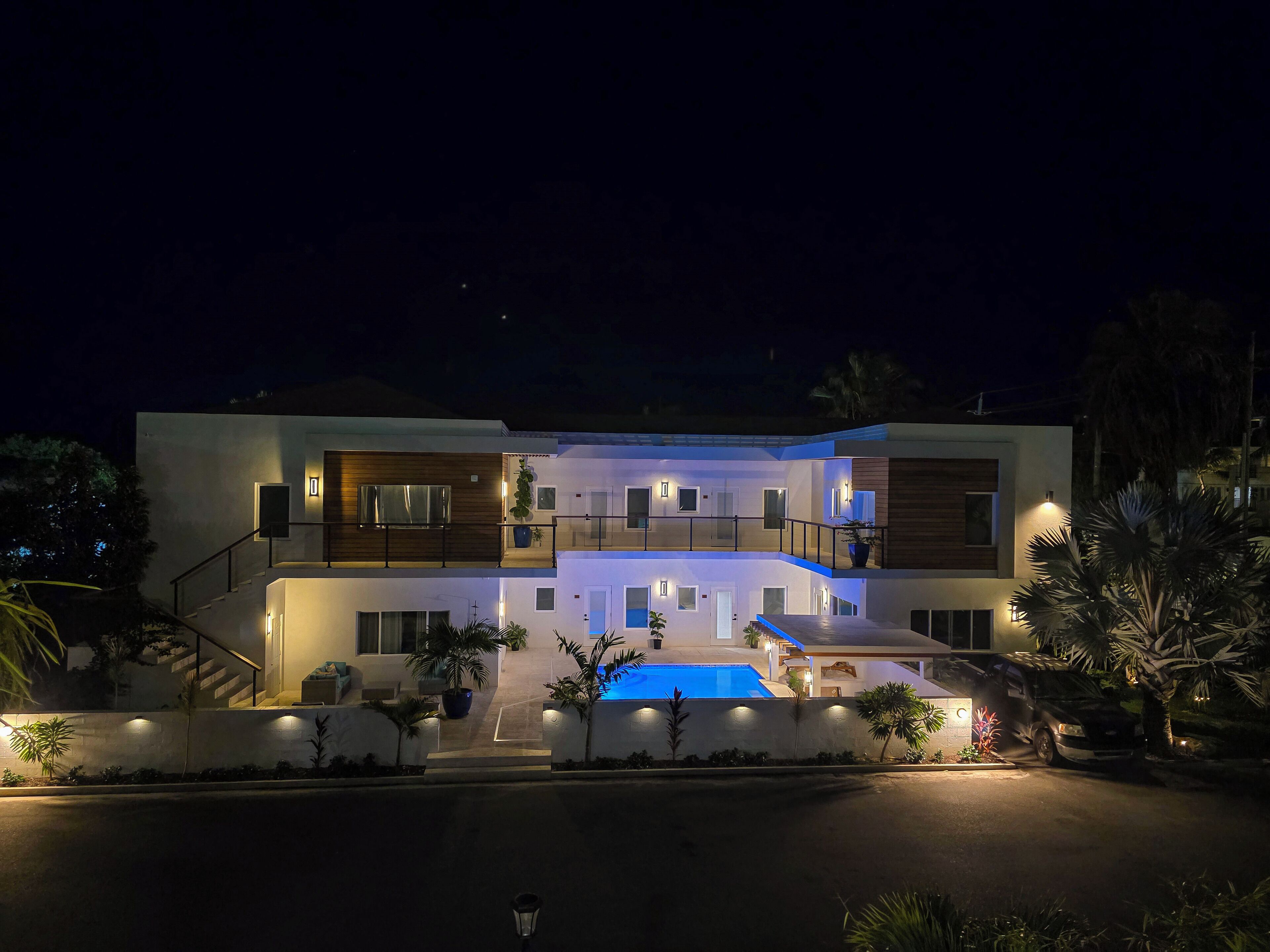 A modern two-story house with a swimming pool, multiple balconies, and outdoor lighting.