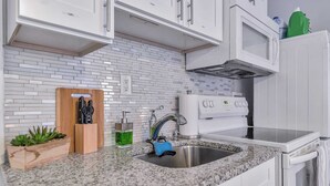 Una cocina moderna con armarios blancos, encimera de granito, pileta de acero inoxidable y microondas.