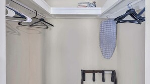 Un armario pequeño y ordenado, con espacio para colgar, un estante y un tablero de planchar fijado a la pared.