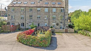 A stone building with multiple windows and a paved driveway. - Bridge End Mill Apartments by Guestz (Settle)