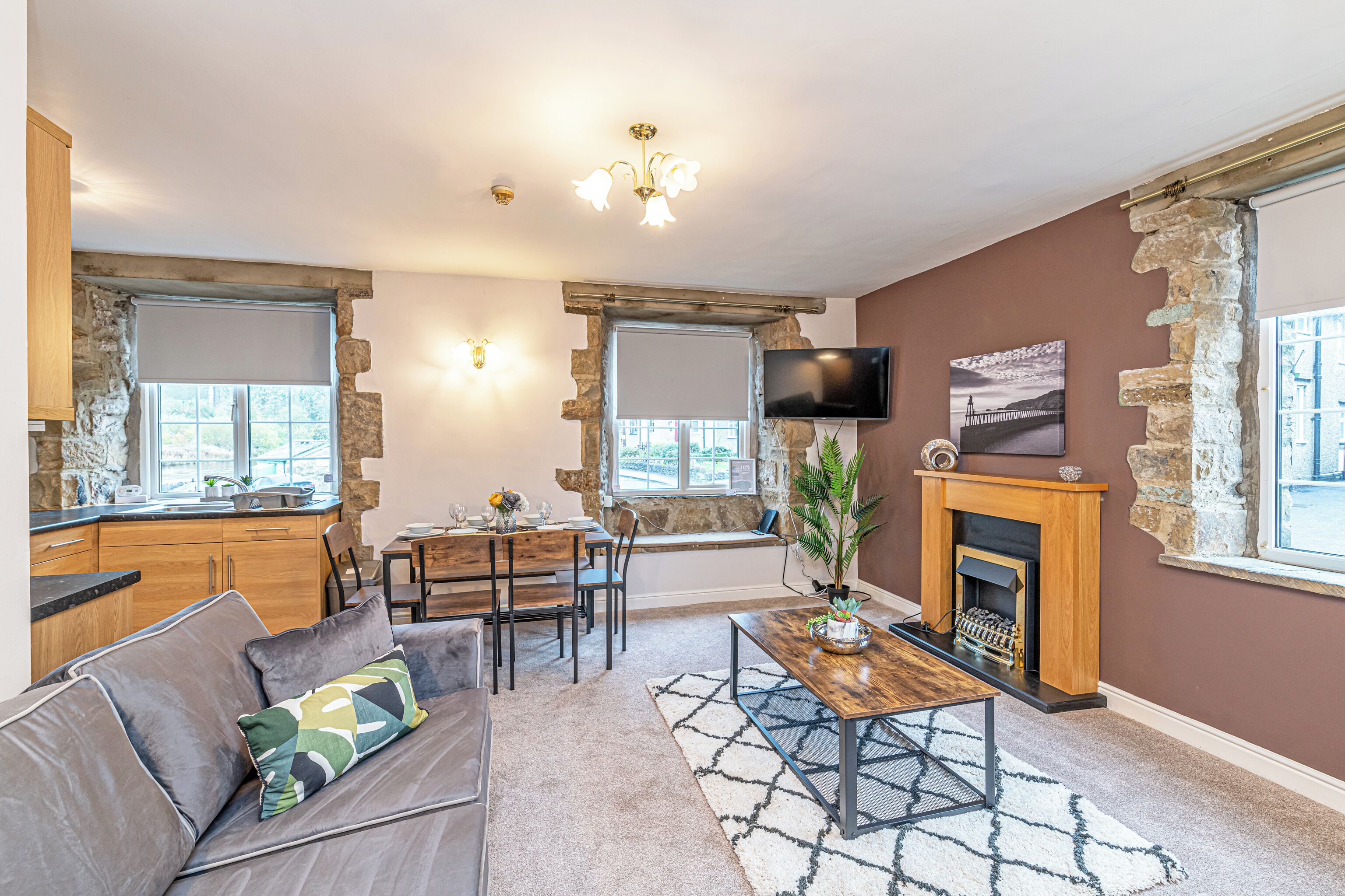 A living room with a stone fireplace, a television mounted on the wall, and a dining area with a table and chairs.