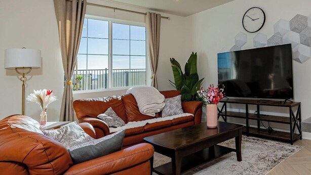 A modern living room with a leather sofa, a coffee table, a TV, and a large window with curtains.
