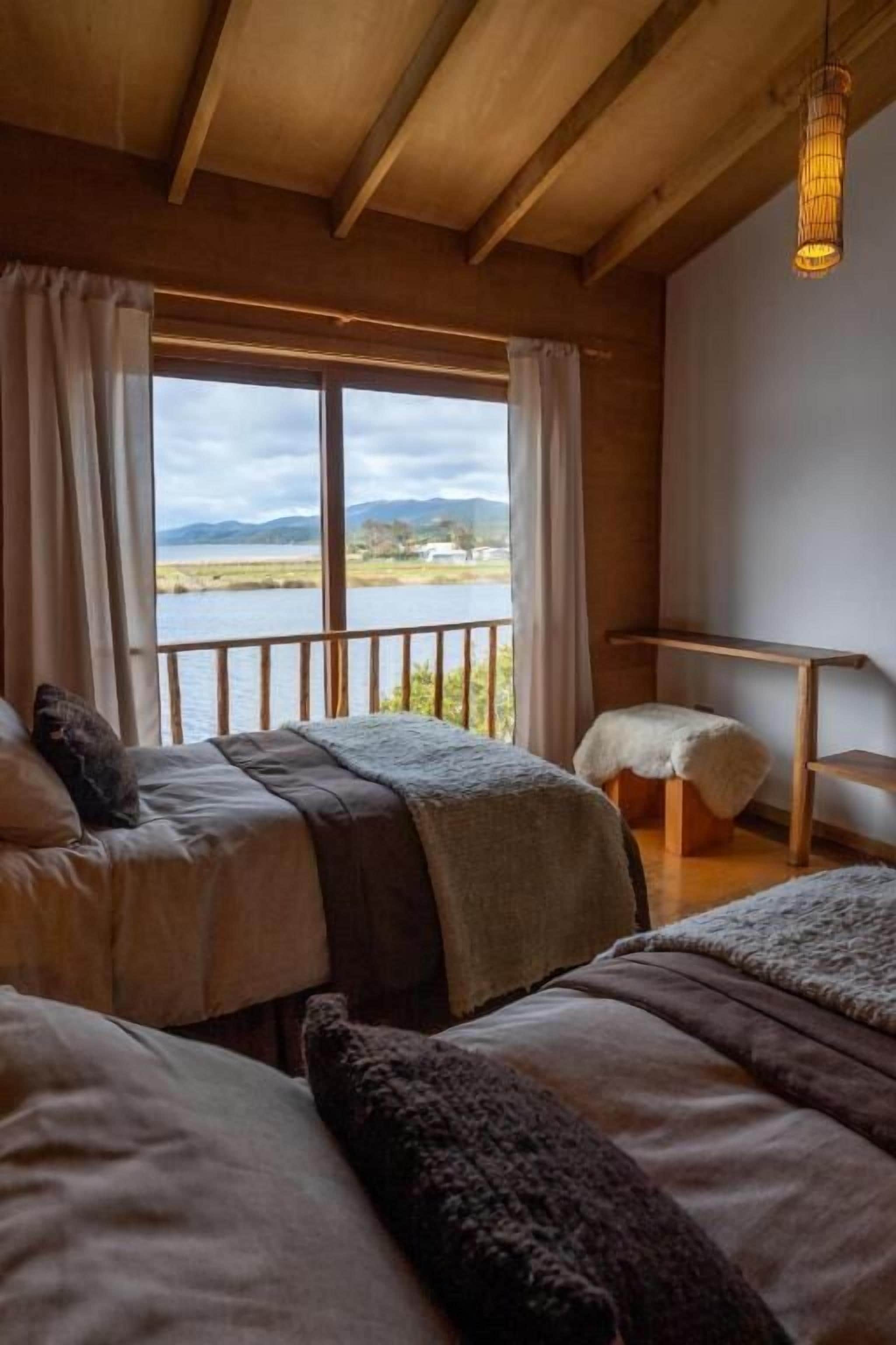 A room with two beds, a view of a lake, and a hanging light fixture.