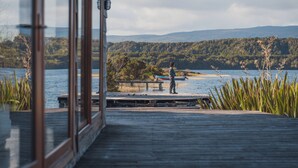 A wooden dock extending into a lake with a person standing at the end. - palafito cucao lodge (Cucao)