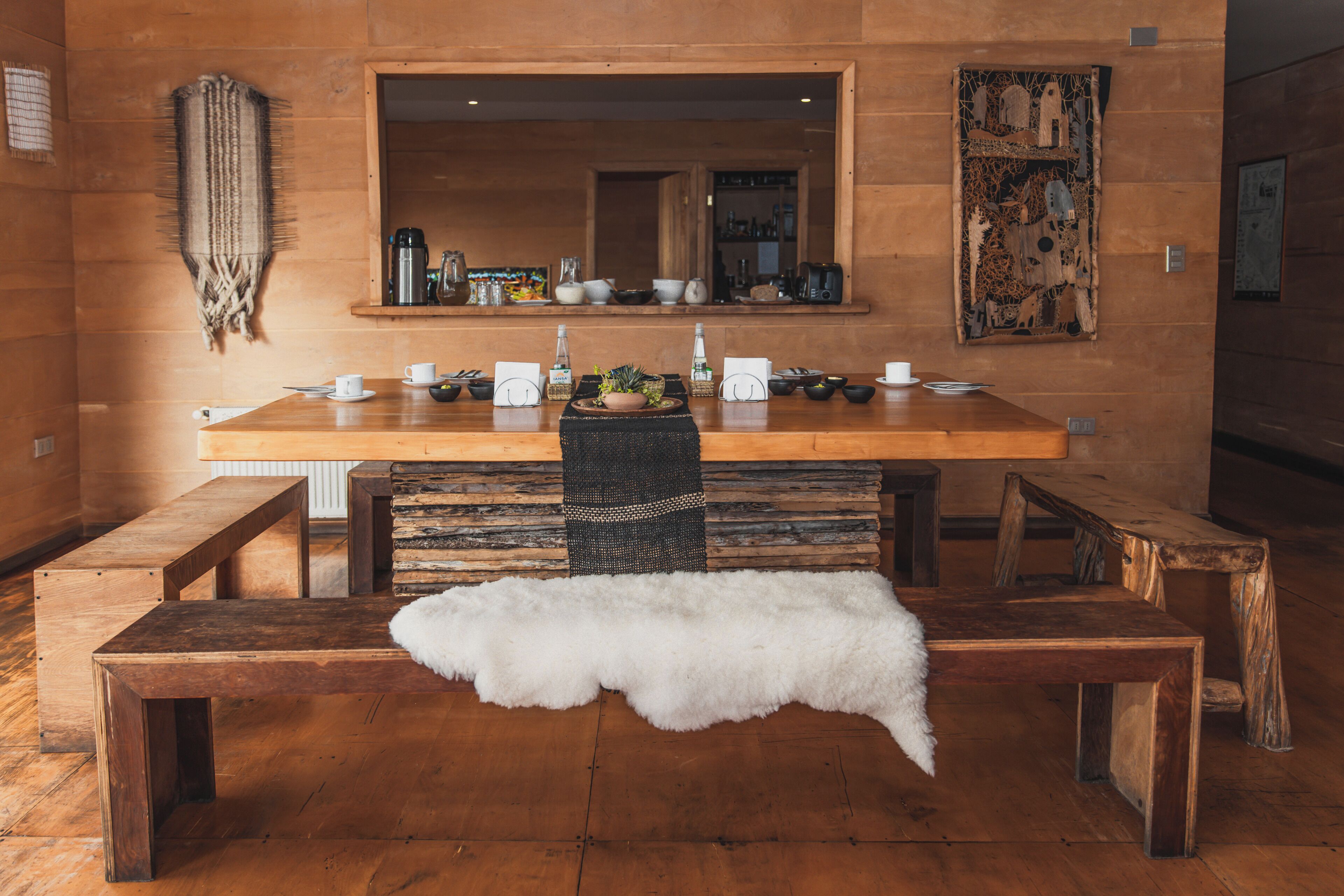 A wooden dining table with benches, a white fur throw, and a mirror above it.