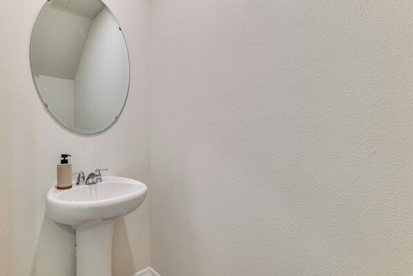 Une salle de bain blanche avec un miroir rond, un lavabo blanc et un distributeur de savon.