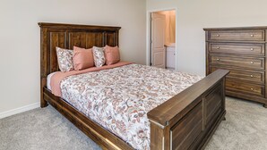 Une chambre à coucher avec un lit en bois, une commode et une porte donnant sur une autre pièce.
