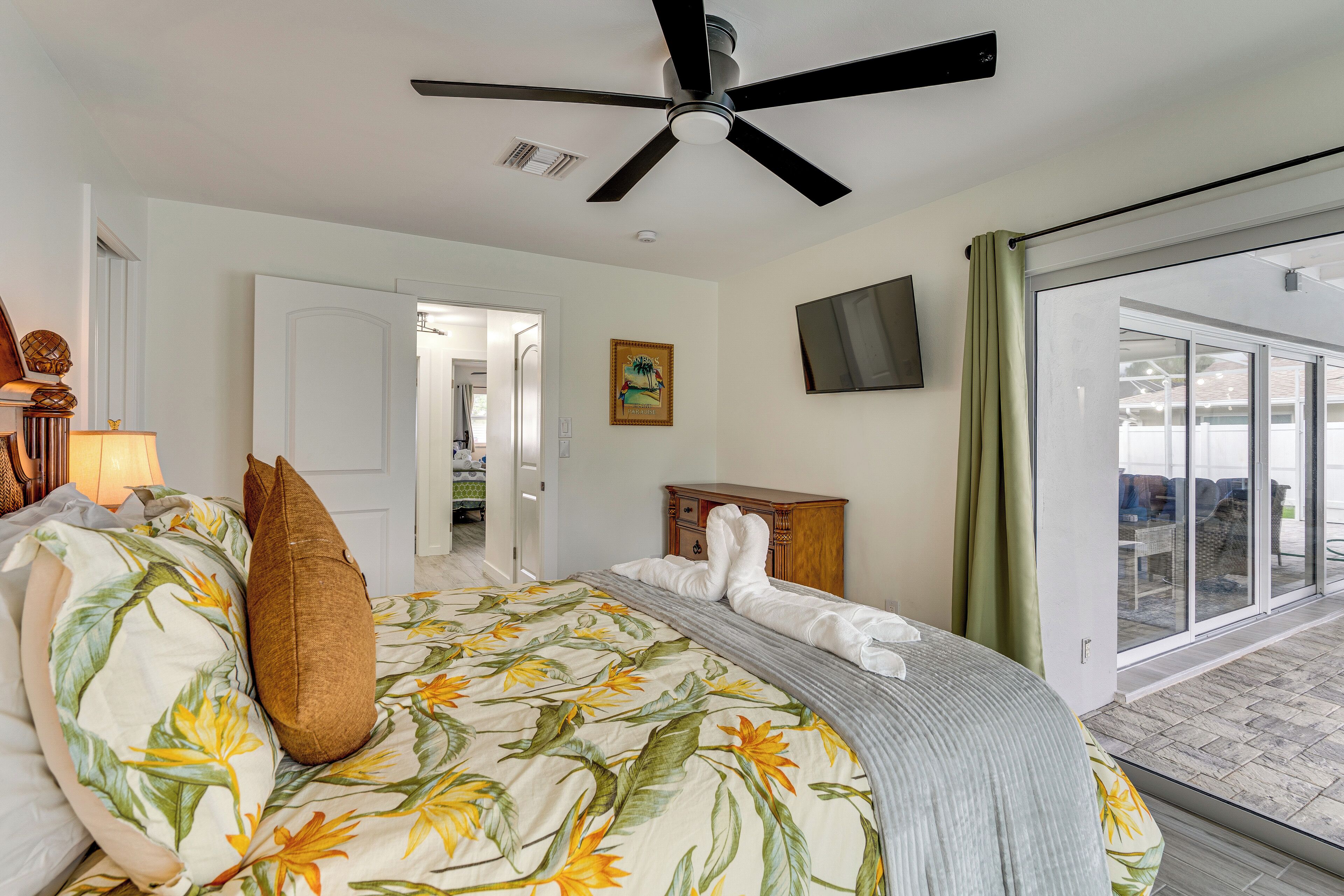 Une chambre d’hôtel équipée d’un lit, d  ’un ventilateur de plafond, d’une télévision et d’une porte-fenêtre coulissante donnant sur l’extérieur.