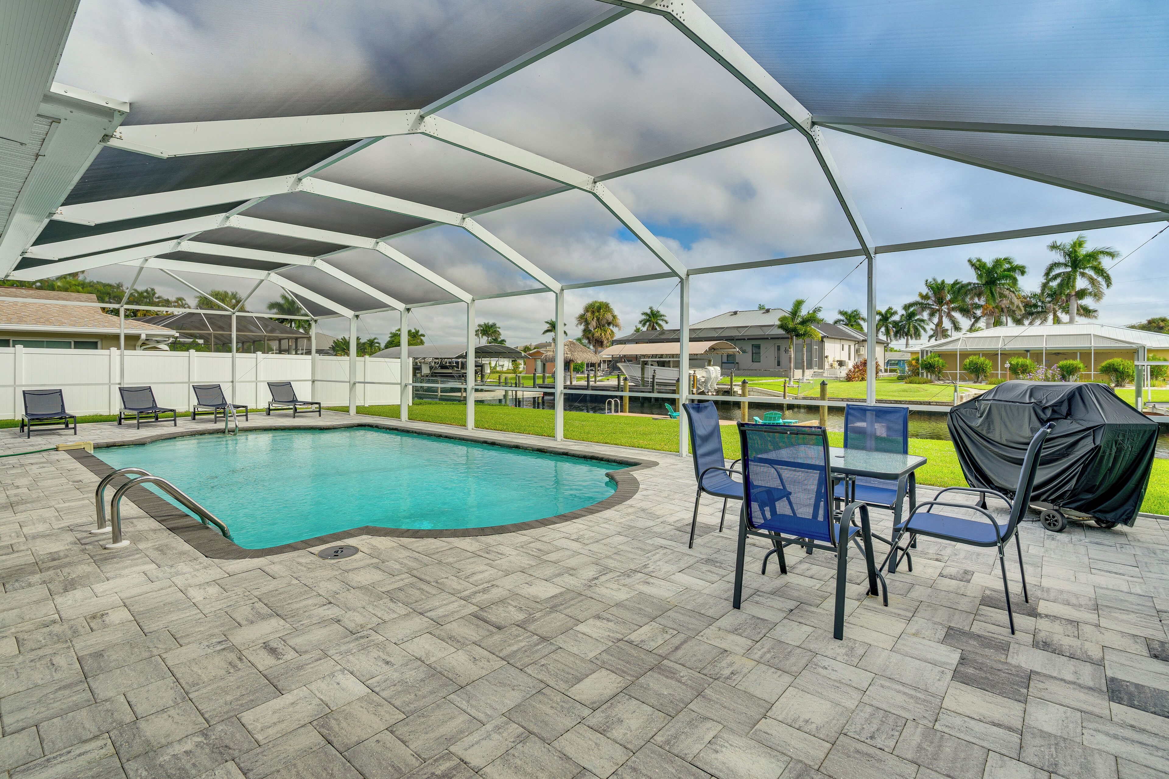 A covered outdoor swimming pool with a tiled deck, lounge chairs, and a table with chairs.