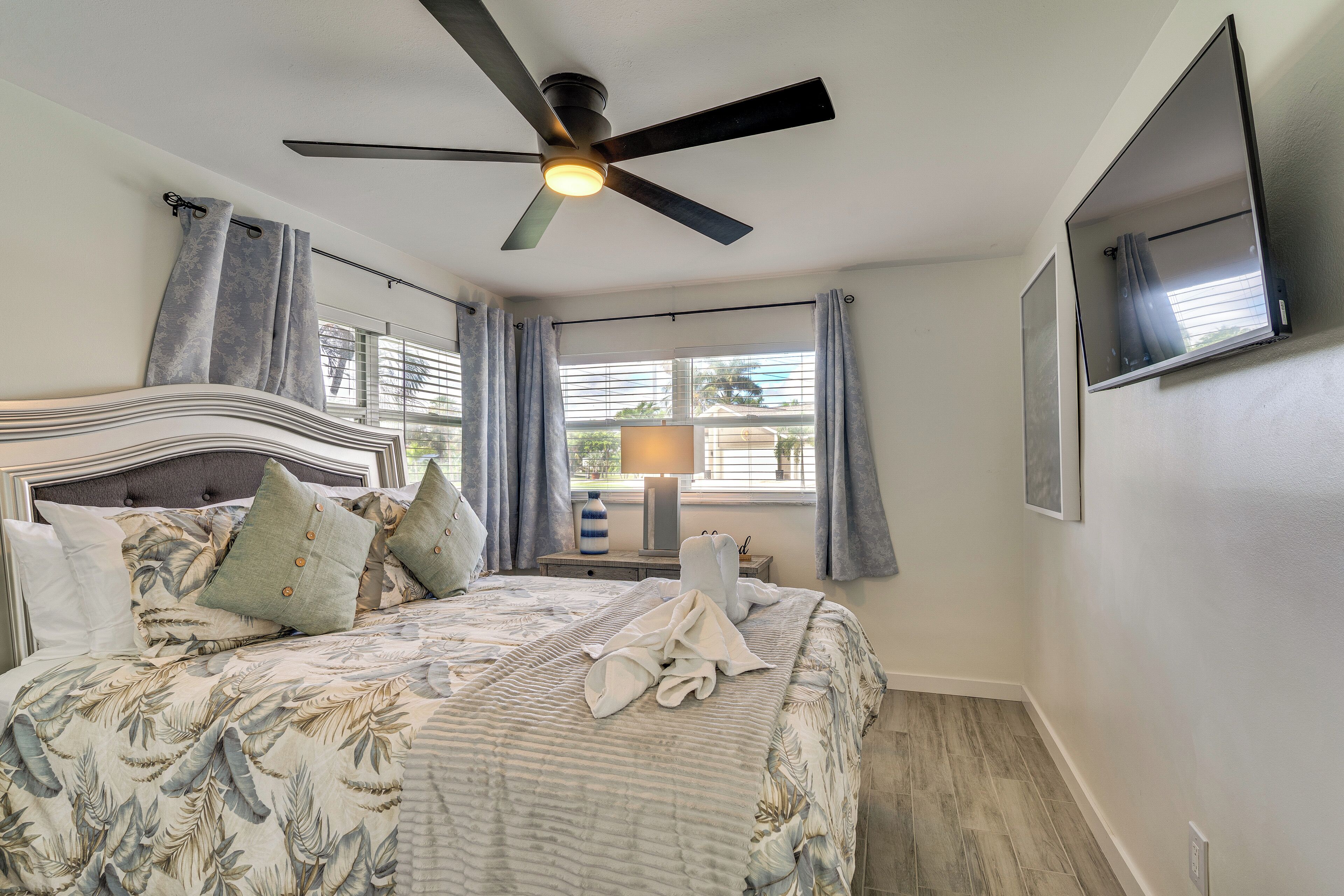A bedroom with a bed, a ceiling fan, a TV, and a window with curtains.