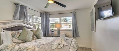 A bedroom with a bed, a ceiling fan, a TV, and a window with curtains.