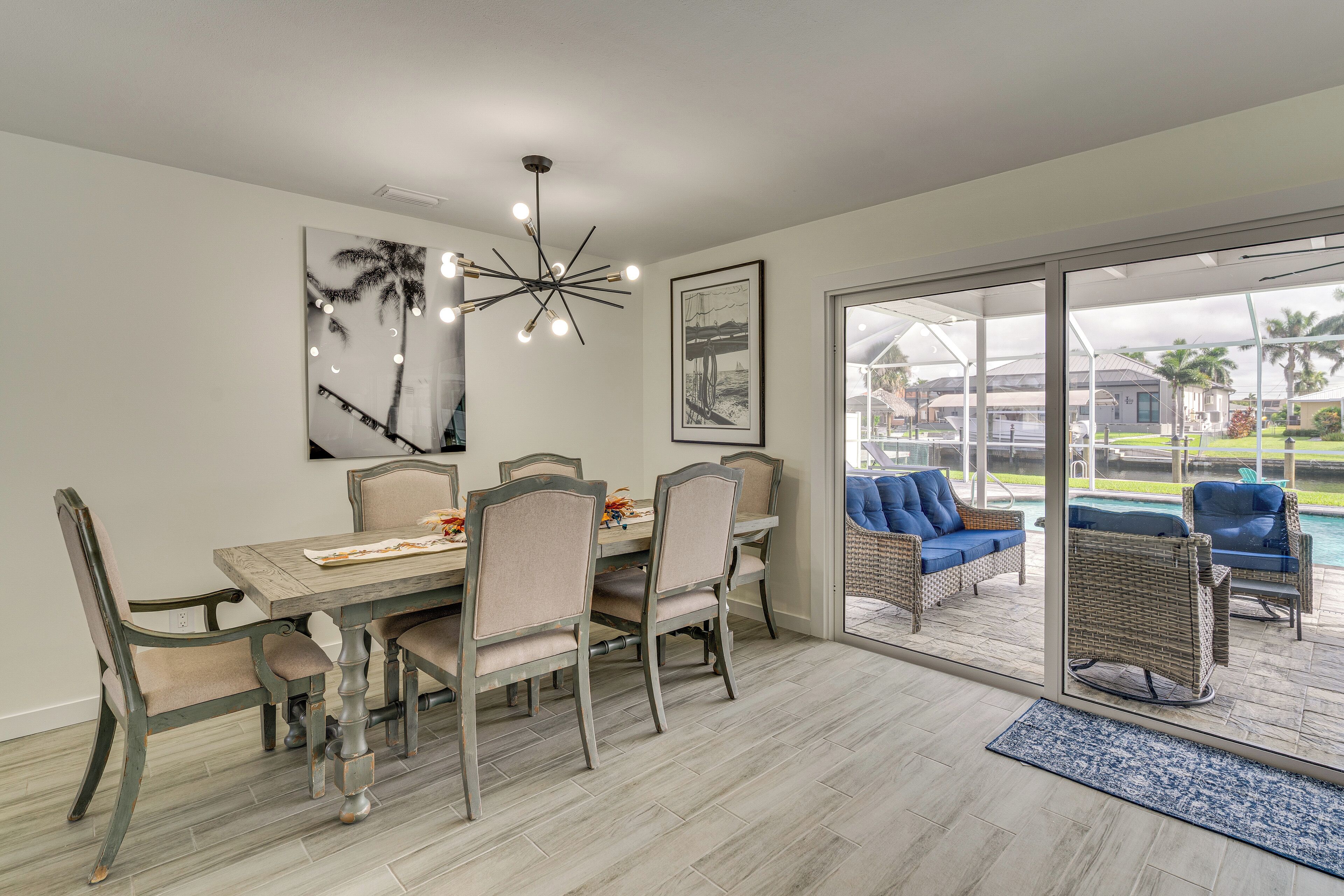 A dining area with a table and chairs, a modern chandelier, and a view of the outdoor patio with seating.