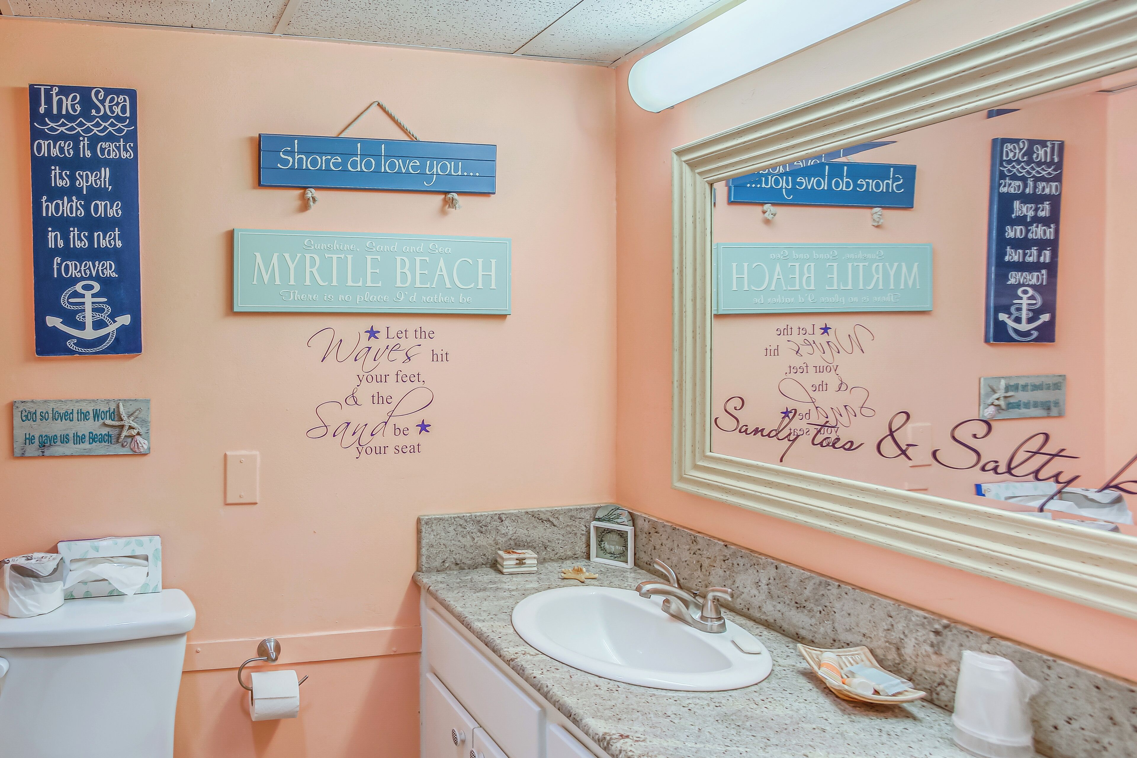 A bathroom with a sink, toilet, and decorative signs on the wall.
