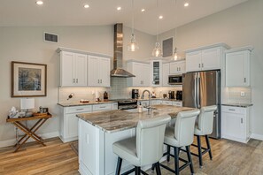 A modern kitchen with white cabinetry, a central island with bar stools, stainless steel appliances, and pendant lighting. - 2 Mi to South Beach: Waterfront Home w/ Lanai! (Marco Island)