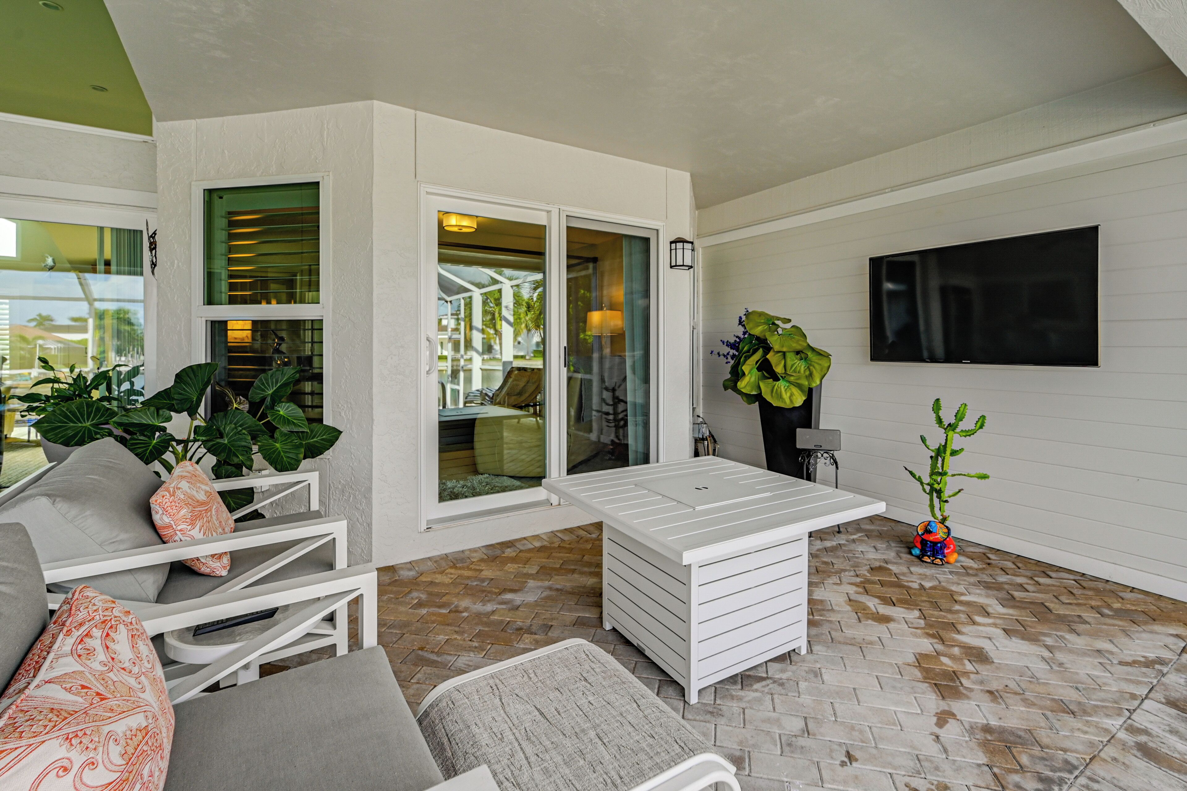 A sunlit patio with a white sofa, a small table, and a TV mounted on the wall.