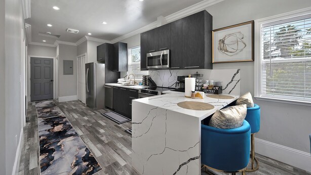 A modern kitchen with dark cabinets, a white marble island, and blue bar stools. - Walk to UC Davis Medical Center! Duplex w/ Patio (Sacramento)