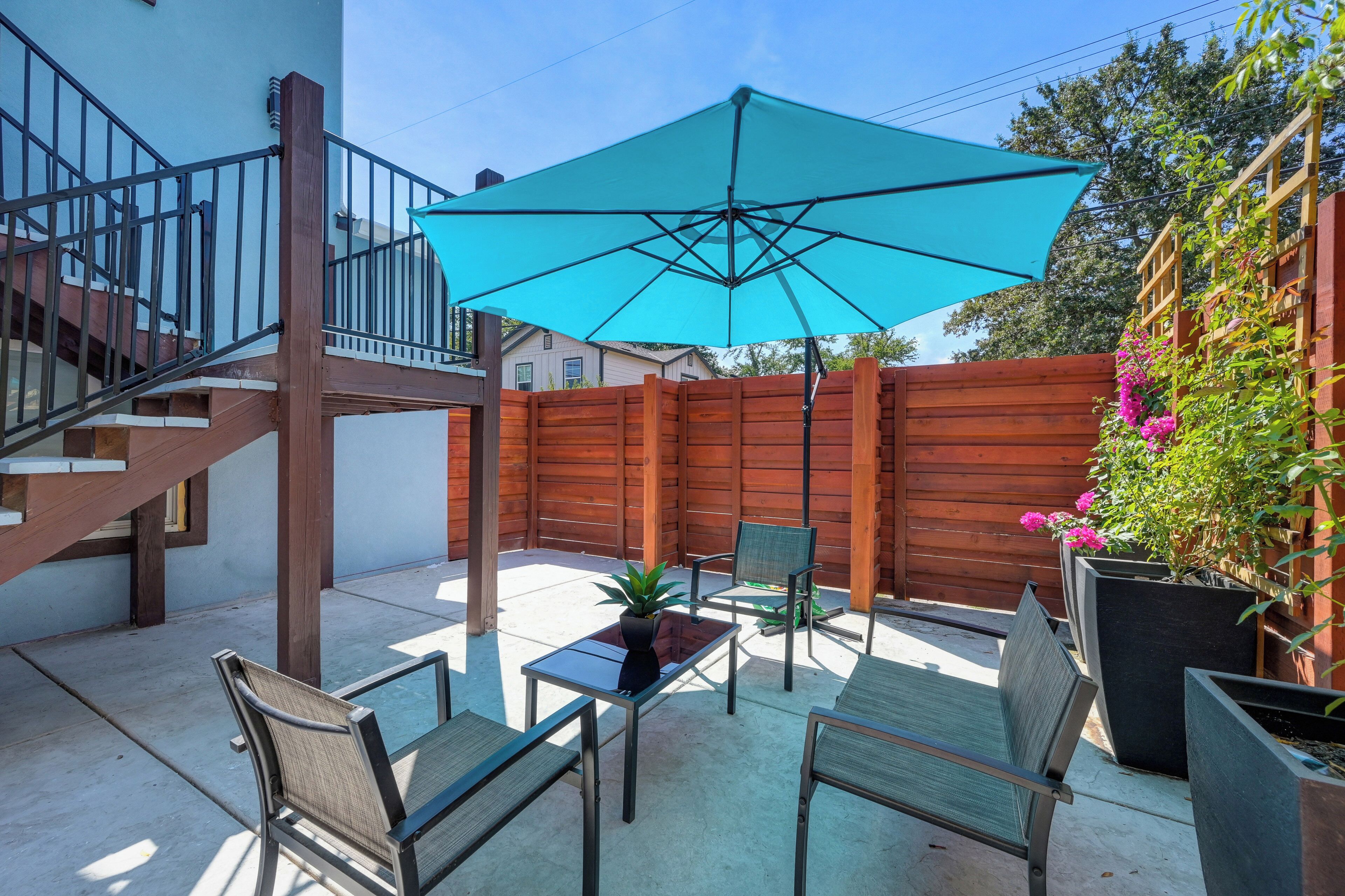 Une terrasse avec une clôture en bois, un parasol turquoise et du mobilier d’extérieur.