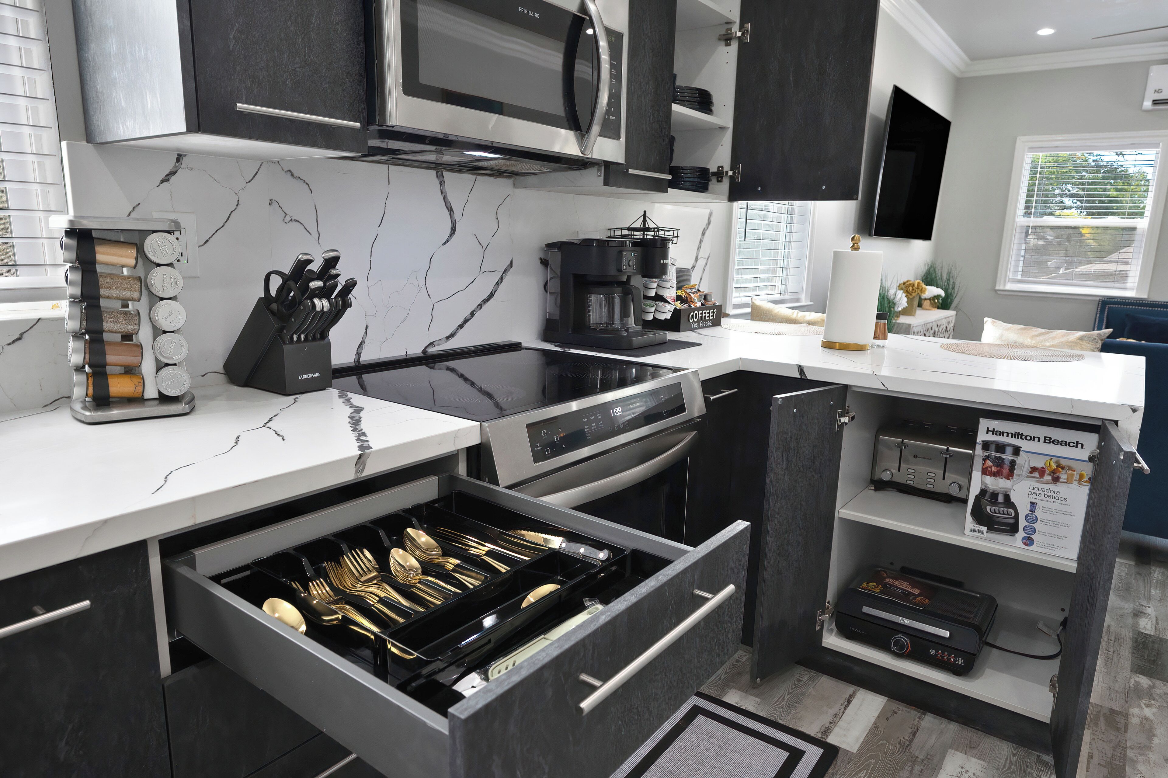 Una cucina moderna con forno integrato, microonde e macchina da caffè. Un cassetto contiene utensili e uno scaffale ospita una macchina per il caffè.