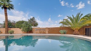 Una piscina limpida circondata da un muro in mattoni, palme e un cielo azzurro terso.