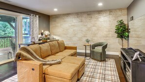 A living room with a beige sofa, a green armchair, a small table with a lamp, and a large window with curtains. - Commuter-friendly Vancouver Rental w/ Yard (Vancouver)