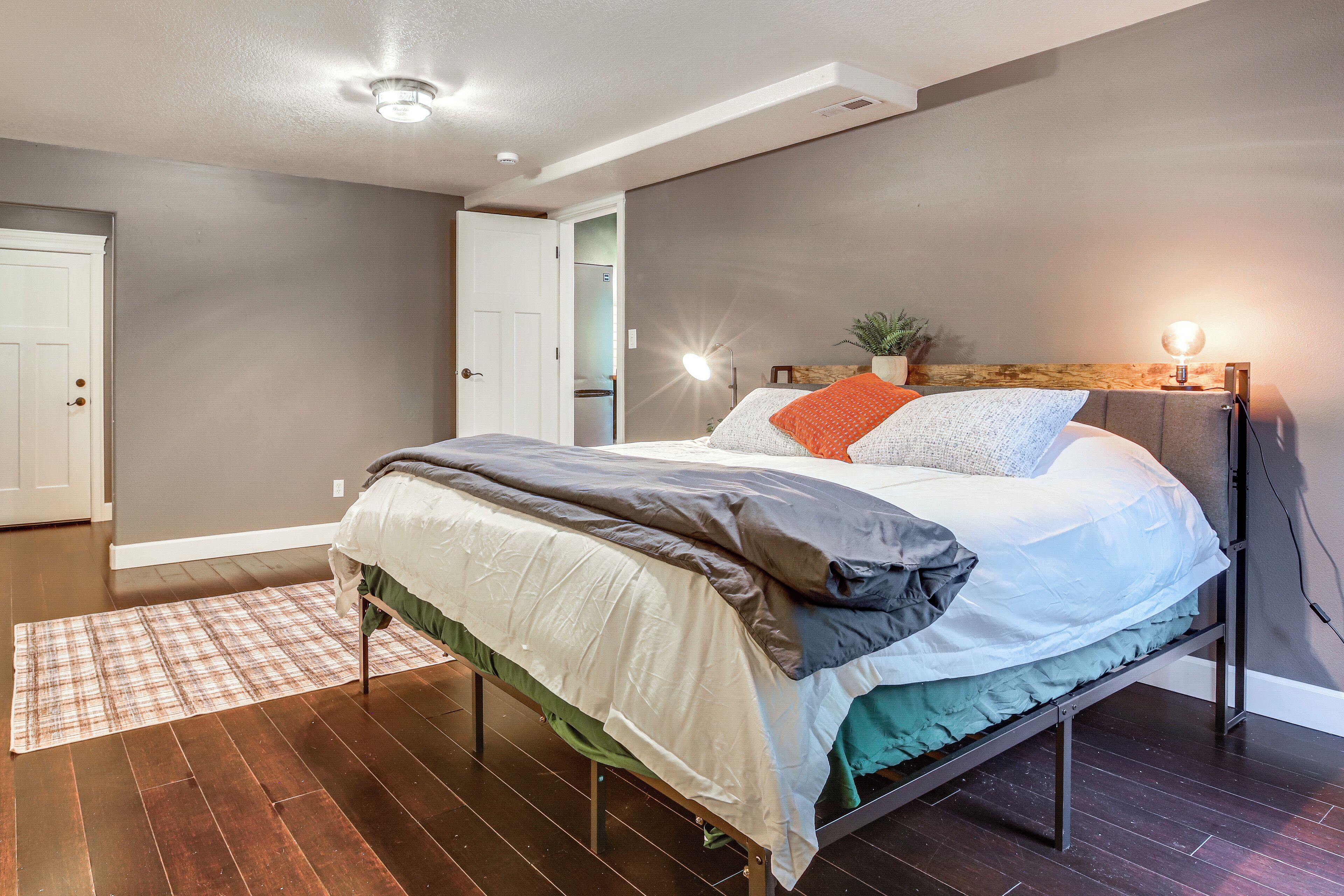 A modern bedroom with a bed, bedside lamps, and a visible door leading to a bathroom.