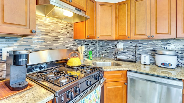 A modern kitchen with wooden cabinets, a gas stove, a coffee maker, a toaster, and a slow cooker. - Quiet Newark Apt Near Colleges, Arenas & Hospitals (Newark)