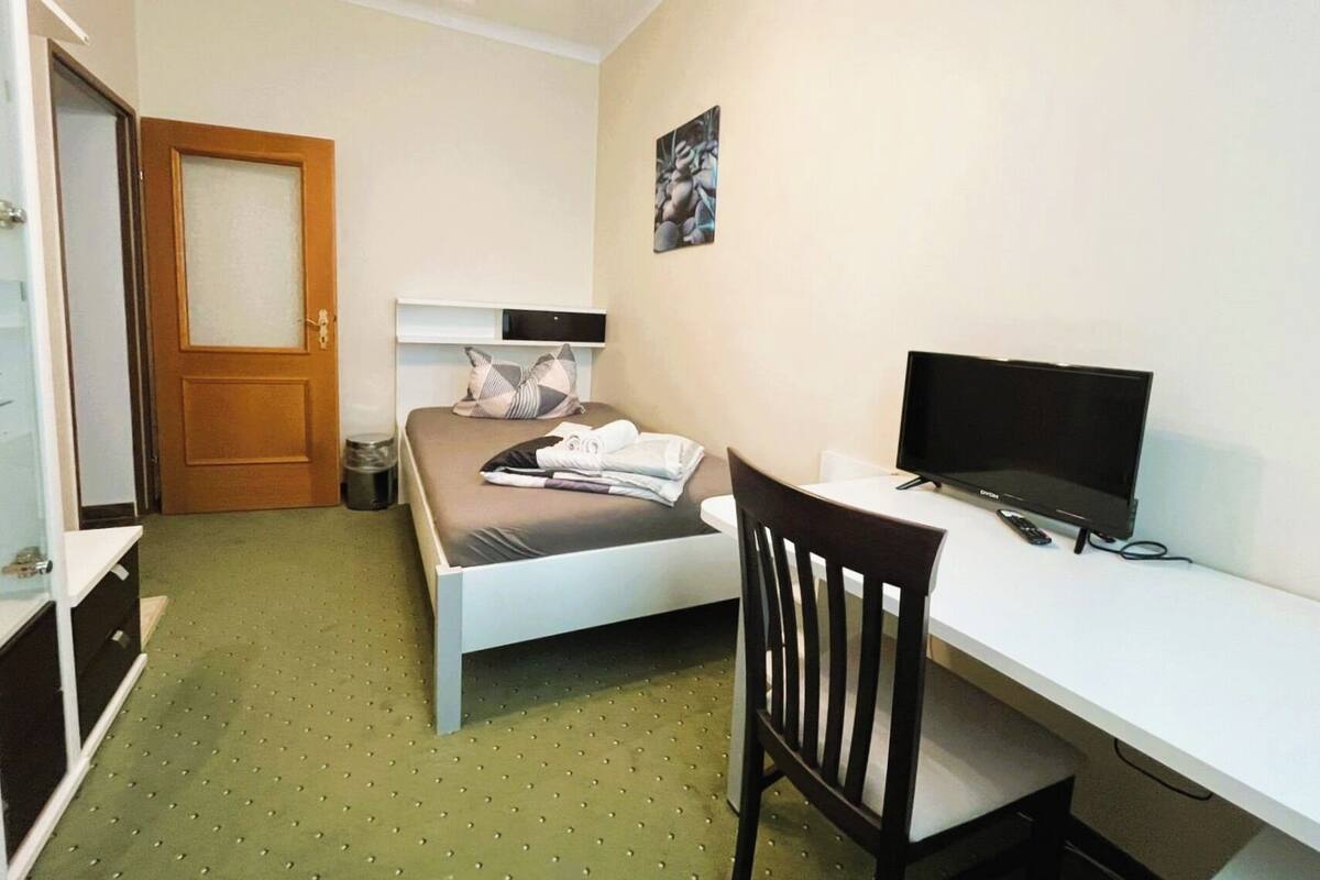 Ein kleines, ordentlich eingerichtetes Schlafzimmer mit Bett, Schreibtisch und Fernseher.