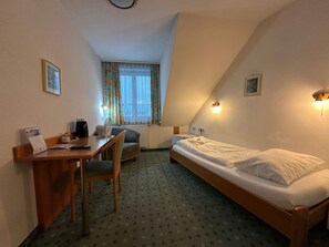 Ein kleiner, gut beleuchteter Raum mit einem Bett, einem Schreibtisch, einem Stuhl und einem fenster mit Vorhängen.