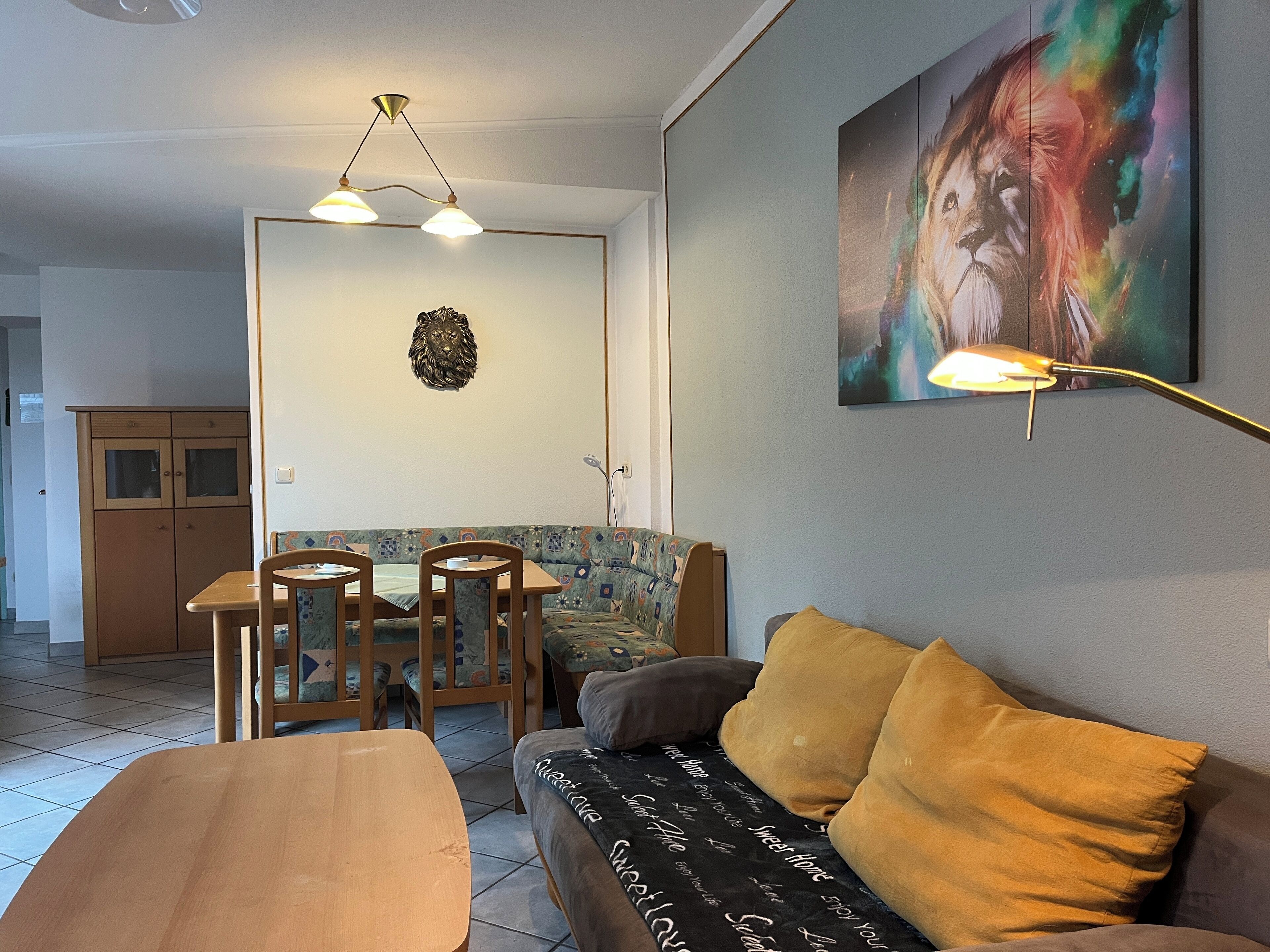 A living room with a sofa, a dining table with chairs, a wall-mounted lamp, and a painting.