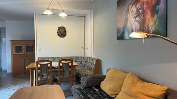 A living room with a sofa, a dining table with chairs, a wall-mounted lamp, and a painting.